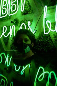 A Man Wearing Face Mask Standing Near a Wall with Neon Sign