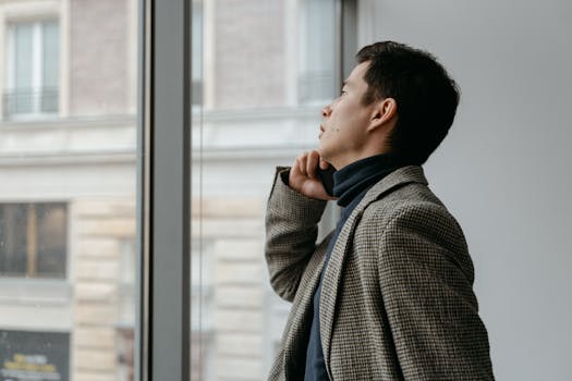 Man in Gray and Black Checkered Dress Shirt Looking Out the Window